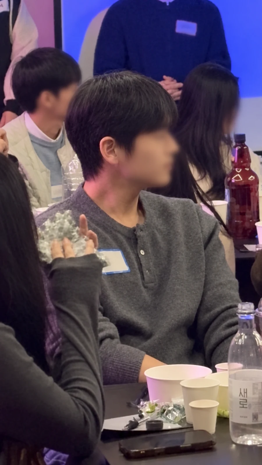 테이블에 앉아 대화하는 참가자들, AI 보정 및 얼굴·명찰 가림 적용